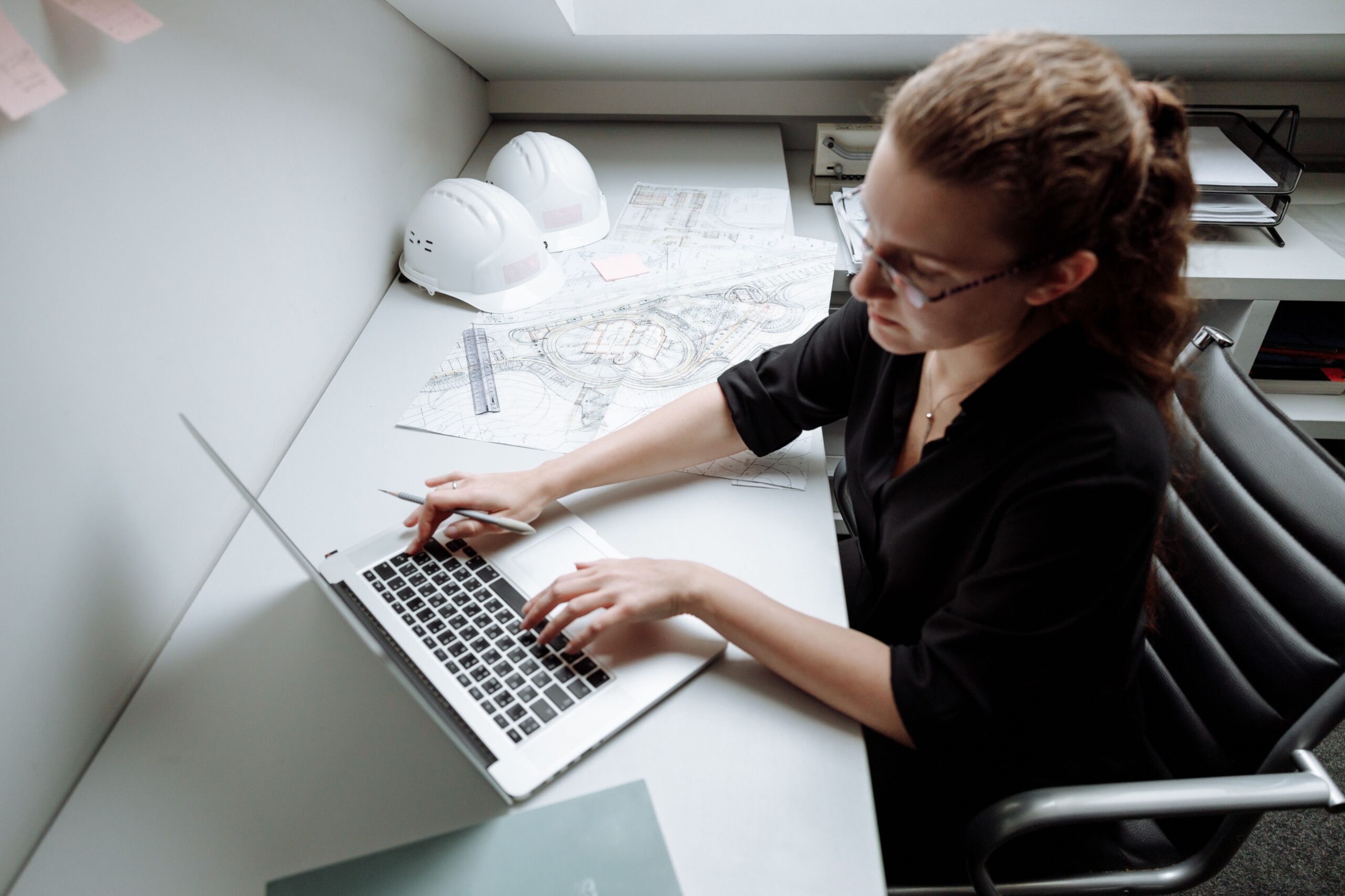 Mujer trabajando con una laptop, con planos y cascos al lado